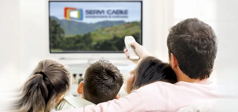 Una familia viendo televisión en casa, con el logotipo de Servi Cable en la pantalla